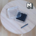 1:12 scale miniature pencil lead case with 11 dark gray leads, clear lidded box shown open on a round wood table