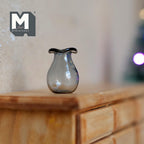 1:12 scale miniature glass pear shaped vase in gray with a dark ruffled rim, shown on a wood dresser