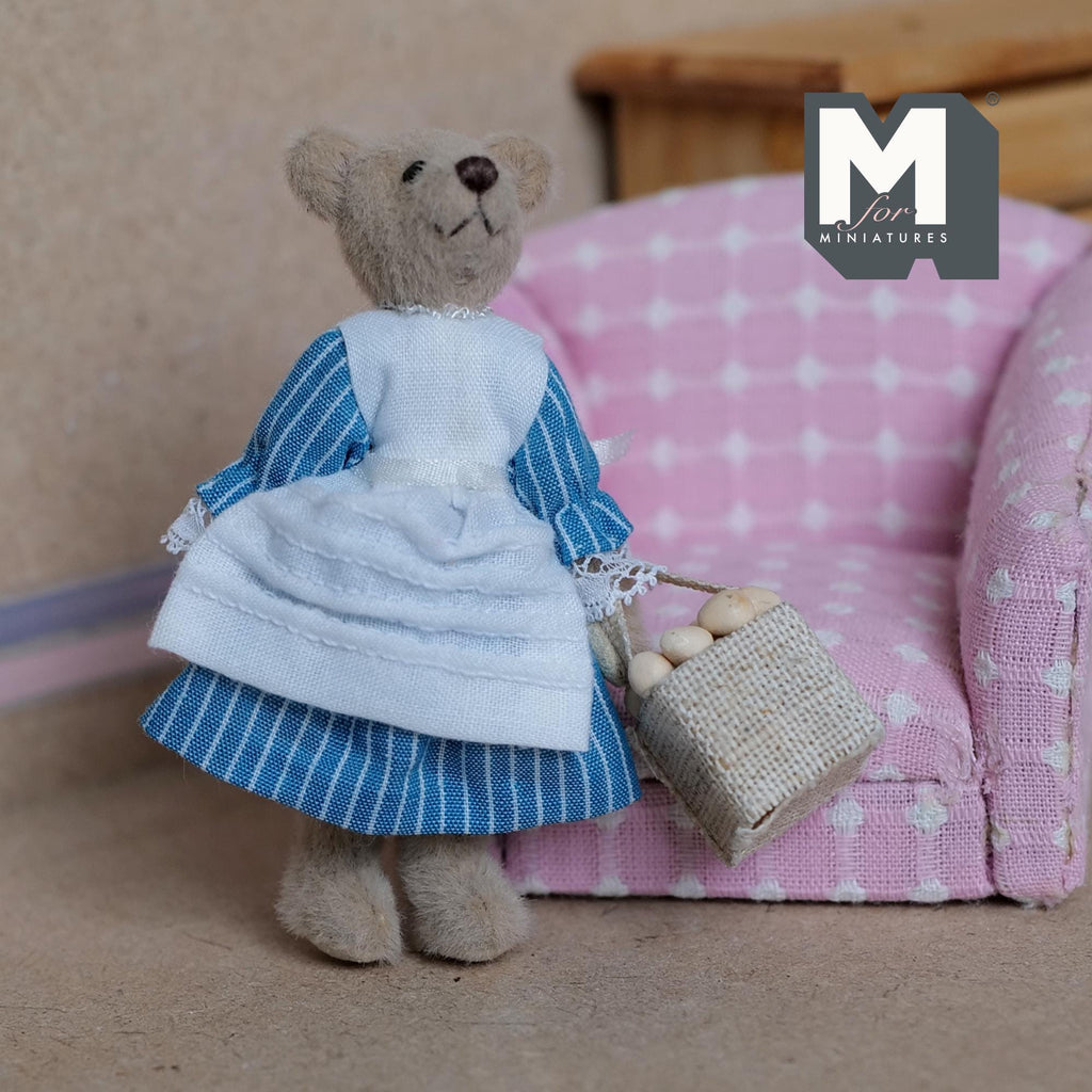 1:12 scale miniature plush lady bear with a basket of eggs, blue gingham dress and white apron, shown by a pink armchair