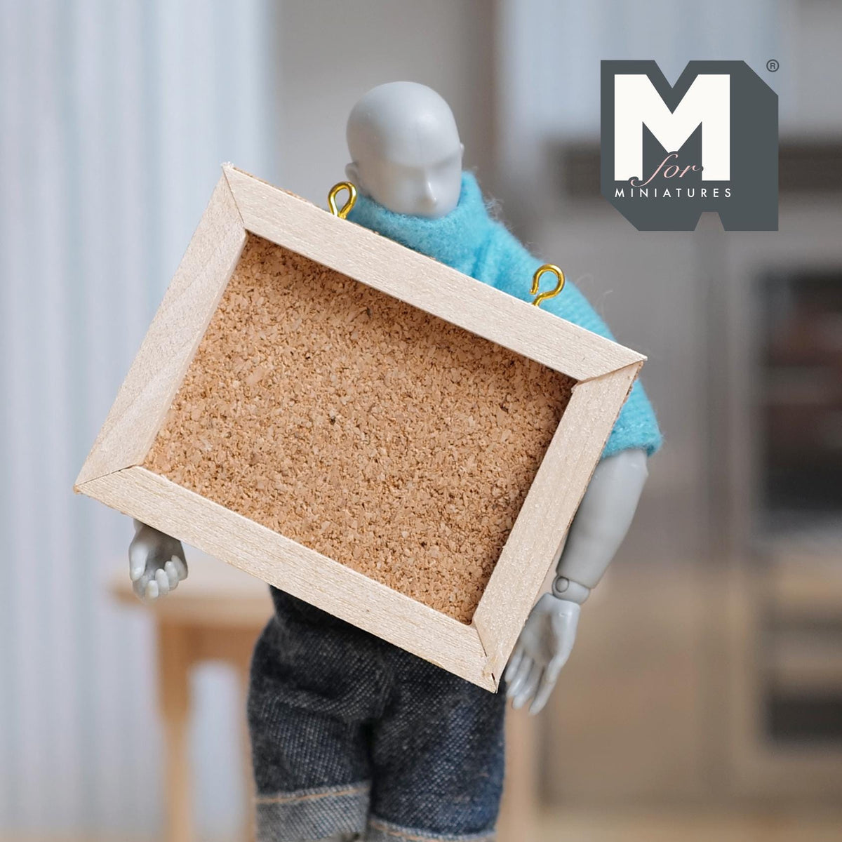 1:12 scale miniature hanging cork board with light wood frame, shown carried by a poseable figure
