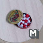 1:12 scale miniature round Santa candy tin filled with red and white candies, lid open, shown on a wood table