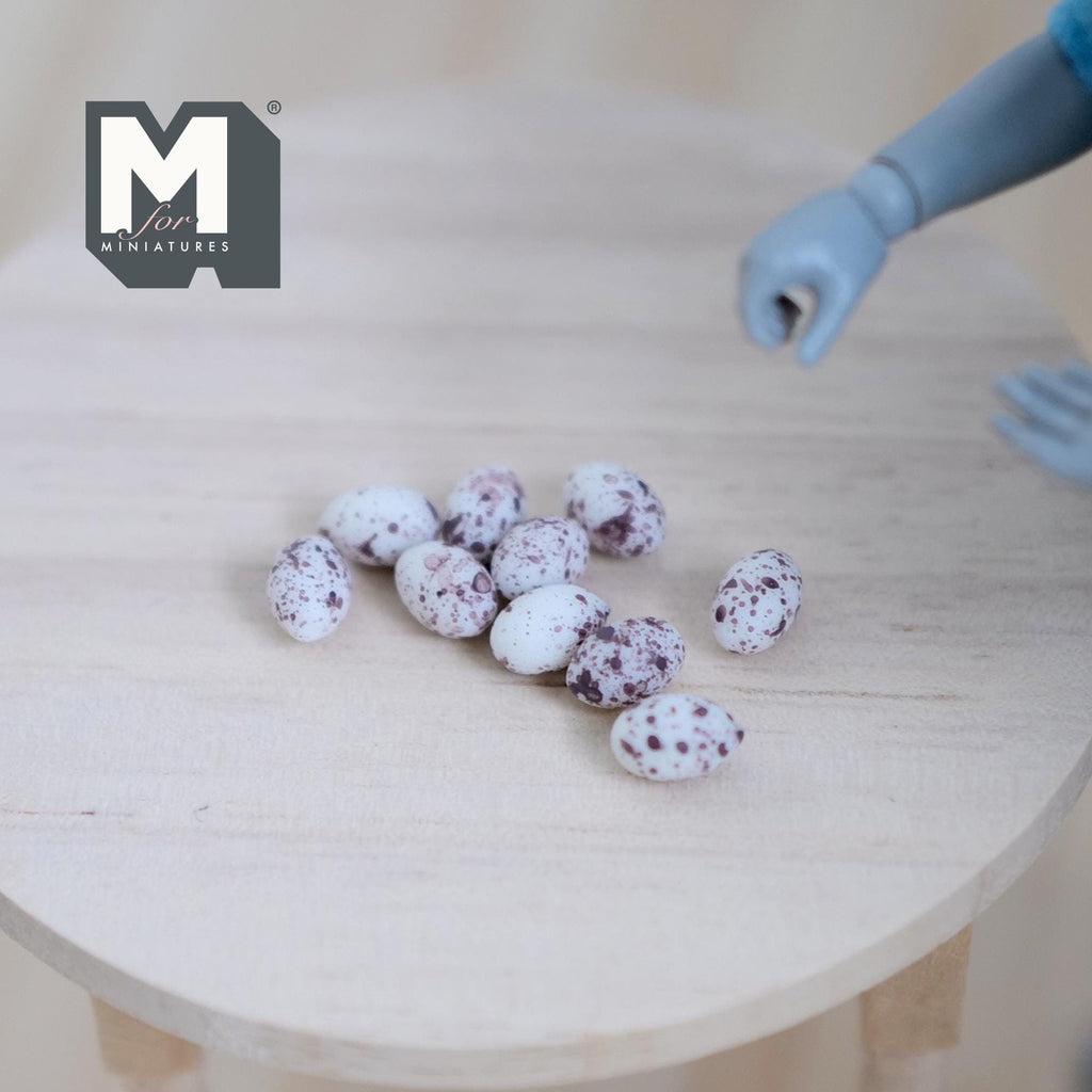 1:12 scale miniature resin quail eggs, set of 10, white with dark speckles, shown on a round wood table