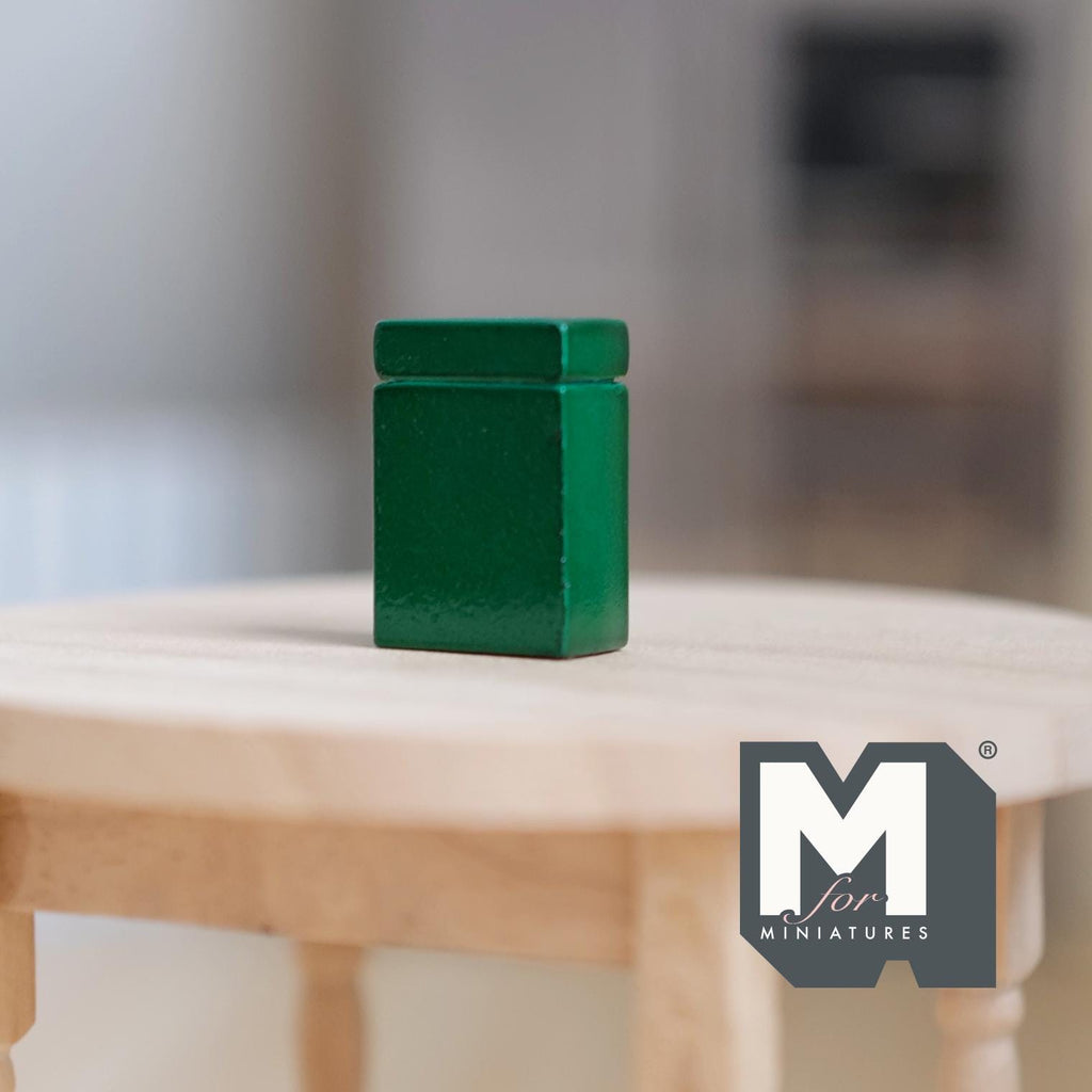 1:12 scale miniature green metal tea tin with lid, square shape, shown on a round light wood table