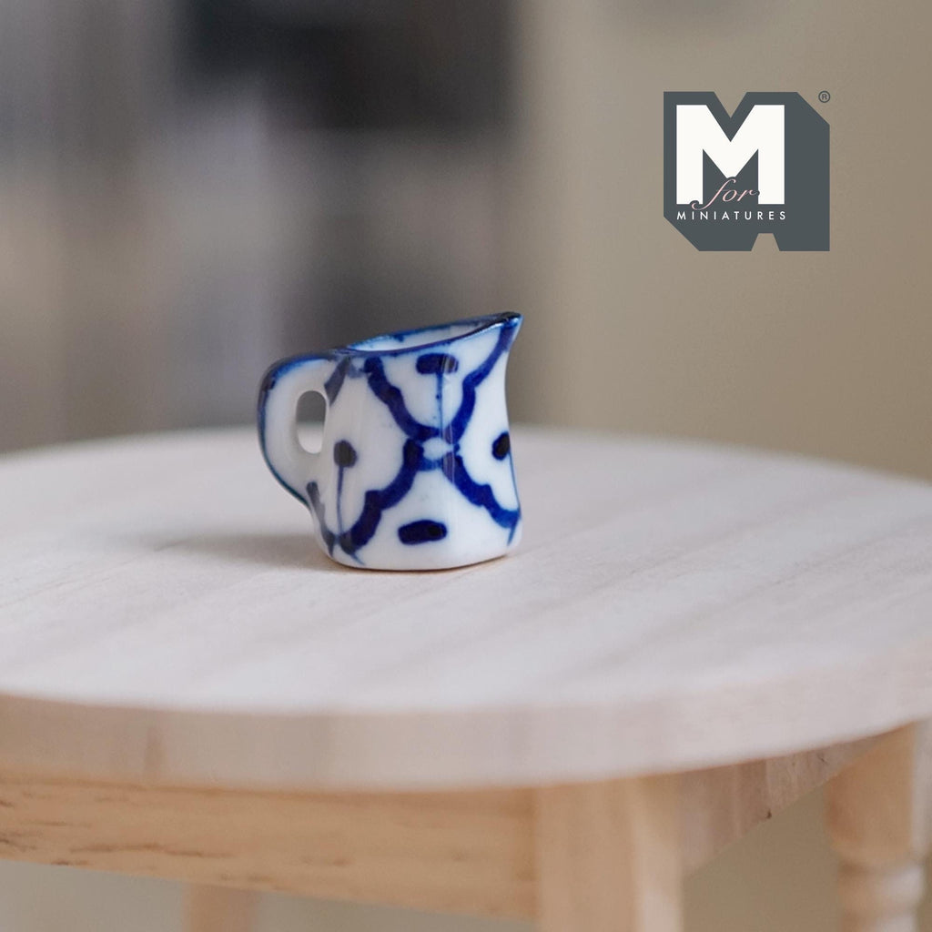 1:12 scale miniature ceramic milk jug with handle, white with hand painted blue pattern, on a round wood table