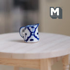 1:12 scale miniature ceramic milk jug with handle, white with hand painted blue pattern, on a round wood table