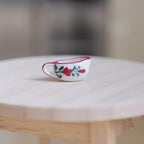 1:12 scale miniature ceramic gravy boat or cream boat in white with red rose pattern and red rim, on a round wood table