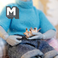 1:12 scale miniature resin kitten lying upside down and playing, orange and white, held in the lap of a poseable figure