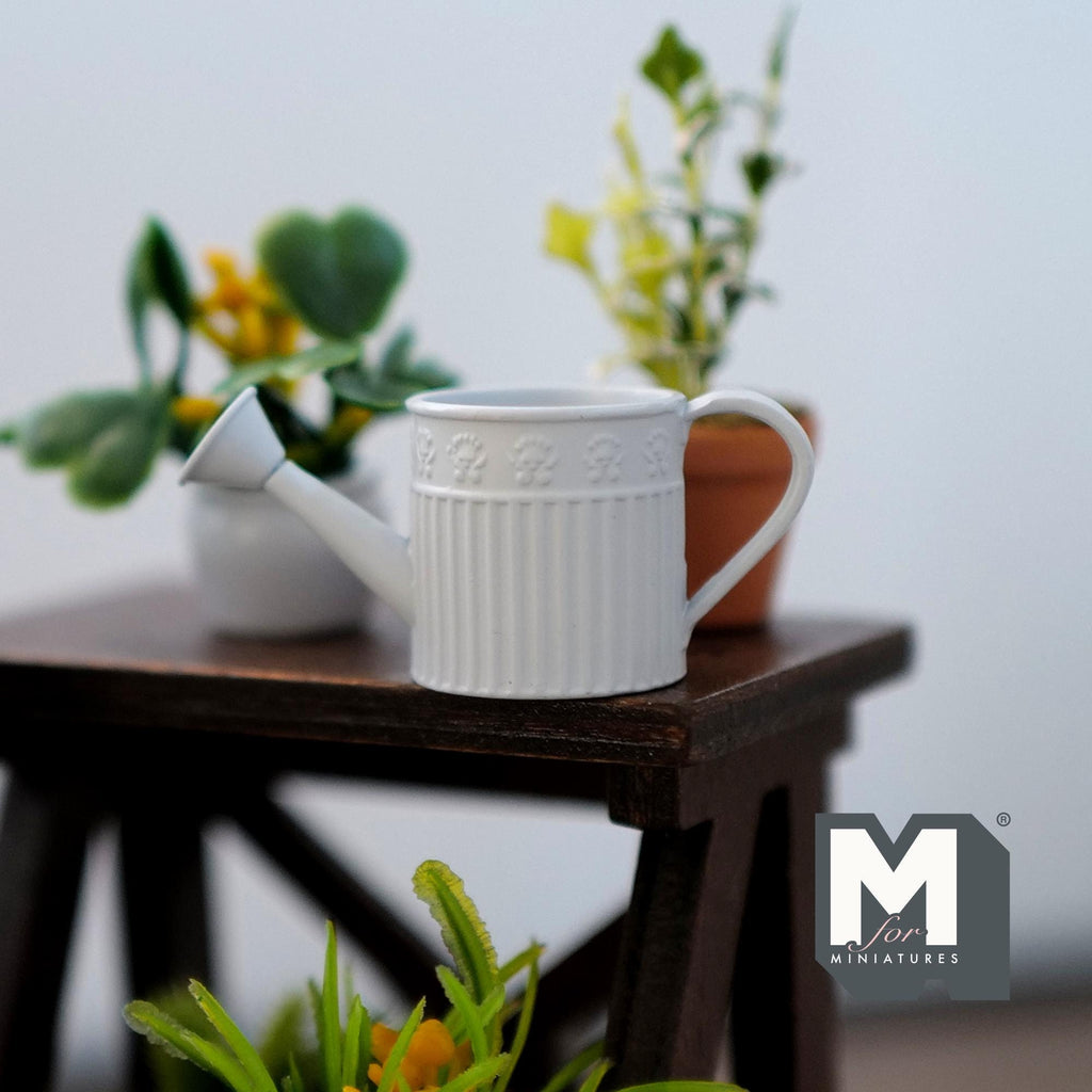 1:12 scale miniature light blue metal round watering can with ribbed body, shown on a dark wood plant stand with plants