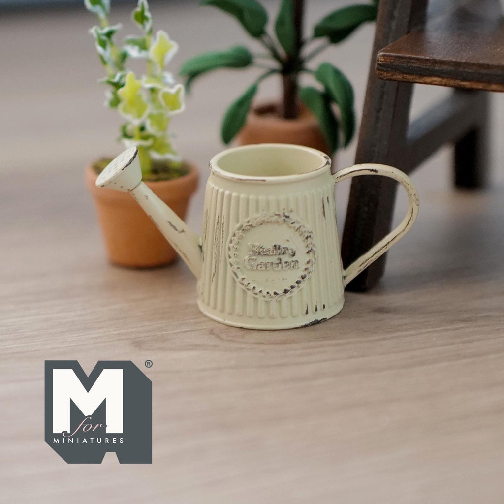 1:12 scale miniature rustic metal watering can in beige with slanted ribbed body and label, beside potted plants