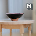 1:12 scale miniature large black clay fruit bowl with flared rim and terracotta foot, shown on a round wood table