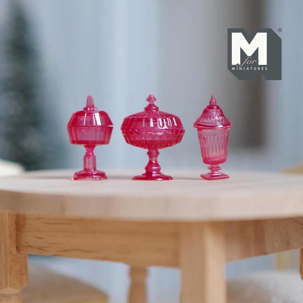 1:12 scale miniature footed candy dishes with lids in clear magenta, set of 3 shapes, on a round wood table