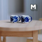 1:12 scale miniature ceramic coffee mugs in white with blue floral pattern, set of 2, on a round wood table