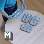 1:12 scale miniature metal baking molds in silver with stars, hearts, donuts and flowers, set of 4, on a round table