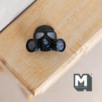 1:12 scale miniature black gas mask wall plaque with 2 round filters, shown lying on a wood surface