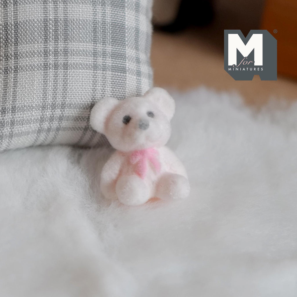 1:12 scale miniature teddy bear cub doll in white flocked finish with a pink bow, sitting on a white fluffy rug