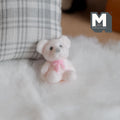 1:12 scale miniature teddy bear cub doll in white flocked finish with a pink bow, sitting on a white fluffy rug