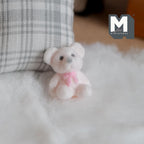 1:12 scale miniature teddy bear cub doll in white flocked finish with a pink bow, sitting on a white fluffy rug