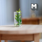 1:12 scale miniature green leafy plant cutting in a clear glass of water, shown on a round wood table