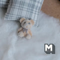 1:12 scale miniature teddy bear cub doll in beige flocked finish with a small bow, on a white rug by a plaid pillow