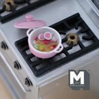 1:12 scale miniature vegetable soup in pink metal pot with lid, shown on a black stove top