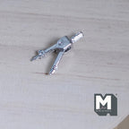 1:12 scale miniature metal drafting compass in silver, shown lying open on a light wood surface