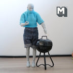 1:12 scale miniature metal charcoal kettle grill in black with lid and 3 legs, shown beside an artist figure