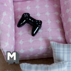 1:12 scale miniature black metal gaming controller, non working, shown on a pink polka dot sofa