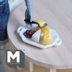 1:12 scale miniature cheese tray with cheese wedges, grapes and knife on a white handled tray, shown on a round wood table