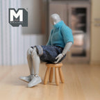 1:12 scale miniature wood kids round stool with 4 splayed legs, natural finish, shown with a seated figure for scale