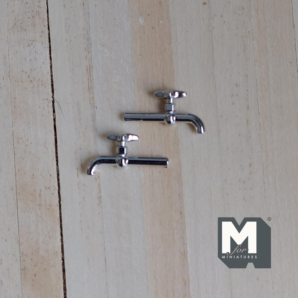 1:12 scale miniature chrome faucets in silver with tap handles, set of 2, shown lying on a light wood surface