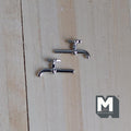 1:12 scale miniature chrome faucets in silver with tap handles, set of 2, shown lying on a light wood surface