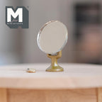 1:12 scale miniature round vanity mirror on a brass stand with comb, shown on a round wood table