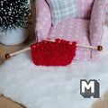 1:12 scale miniature knitting needles with a red knitted piece, shown on a white fluffy rug beside a pink armchair