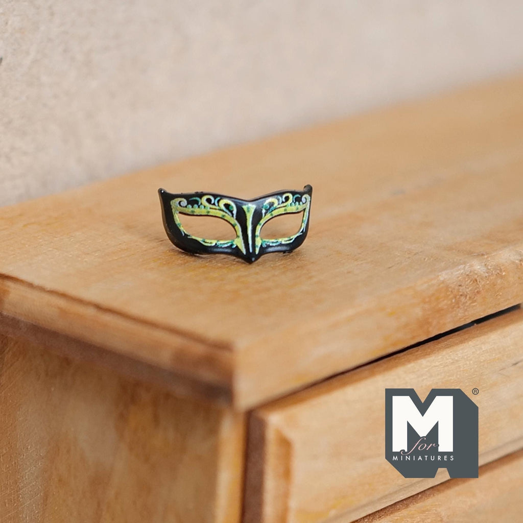 1:12 scale miniature Venetian style half mask wall plaque in black and gold with green accents, shown on a wood dresser