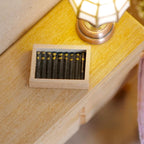 1:12 scale miniature wood cigar box filled with a row of dark cigars, shown on a desk beside a lamp