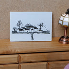 1:12 scale miniature village houses and trees sketch print on a wood backing, shown on a dresser beside a lamp