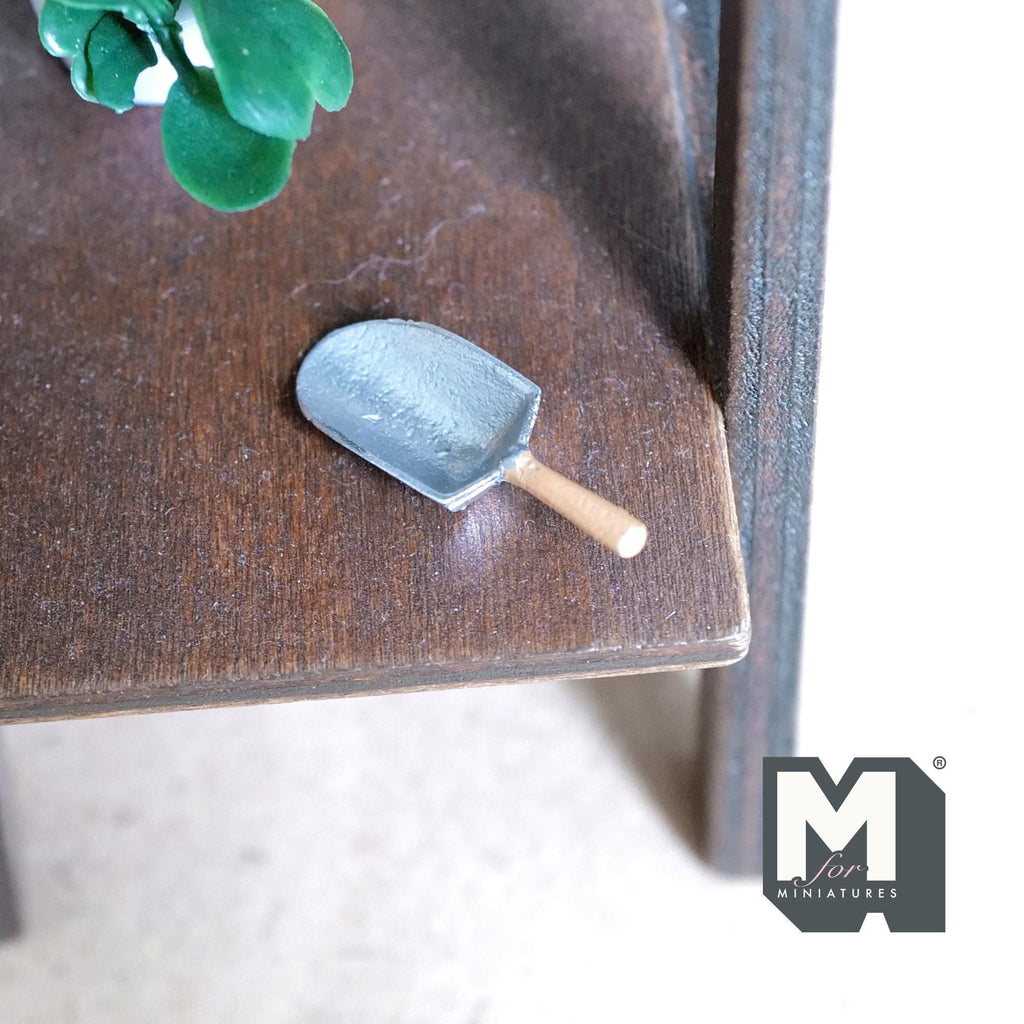 1:12 scale miniature metal flour scoop in silver with wood handle, shown on a dark wood shelf