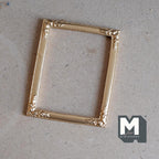1:12 scale miniature resin large ornate picture frame in gold with decorated corners, shown empty on a tan surface