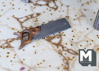 1:12 scale miniature metal hand saw with a brown wooden handle, shown lying on a marble pattern surface