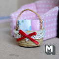 1:12 scale miniature woven rope basket with folded linens, lace trim and red bow, shown by a pink armchair