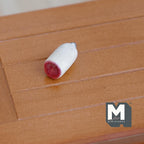 1:12 scale miniature small salami with white casing and red cut end, shown on a wood plank table