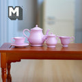 1:6 scale miniature metal tea set in pink with teapot, cup, saucer, milk jug and sugar bowl, set of 5, on a wood table
