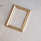 1:12 scale miniature cast resin large picture frame in champagne gold with stepped profile, shown empty on a tan surface