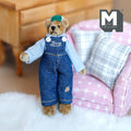 1:12 scale miniature plush bear in denim overalls, checked shirt and green cap with movable limbs, by a pink armchair
