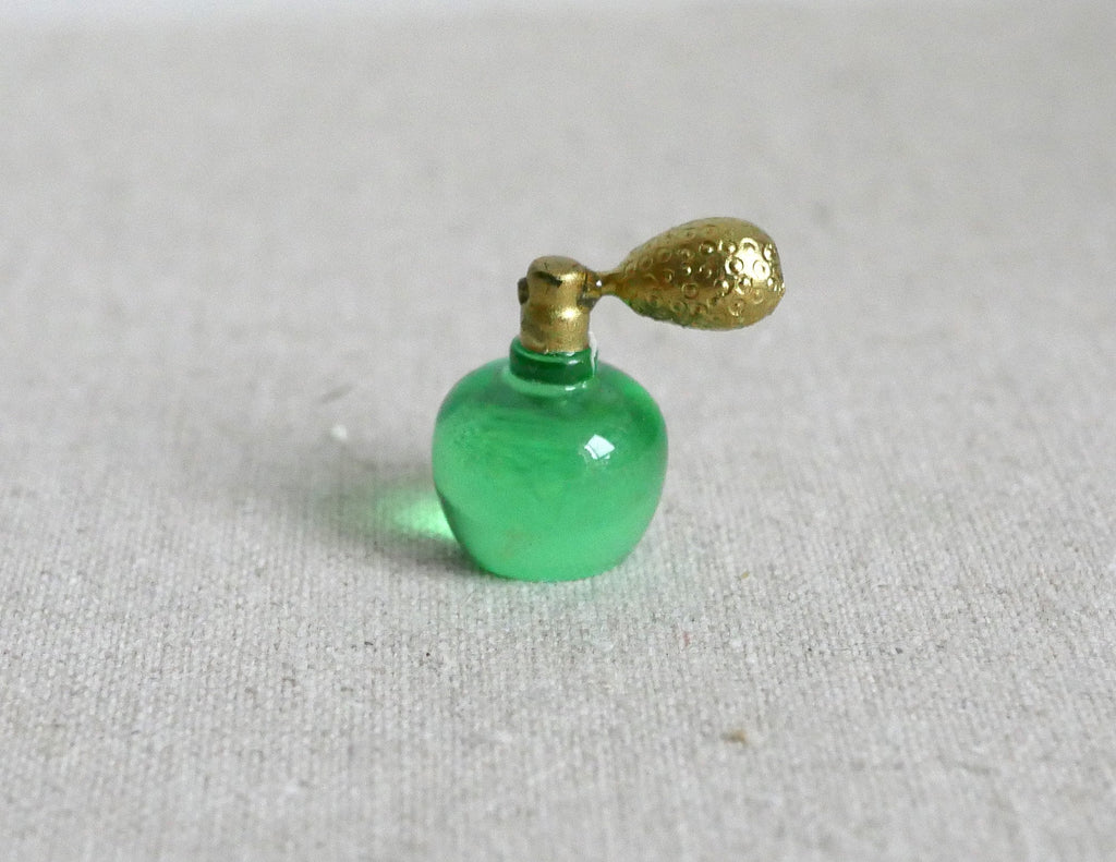 1:12 scale miniature perfume bottle in green with a gold atomizer bulb, shown on a linen surface