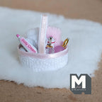 1:12 scale miniature bathroom basket in pink and white with towels and perfume bottles, on a white fur rug