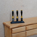 1:12 scale miniature metal beer tap tower in black with 3 handles and gold bands, shown on a wood dresser