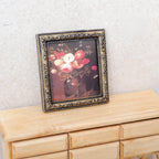 1:12 scale miniature framed rose painting in ornate gold frame, pink and red blooms on dark ground, on a wood dresser