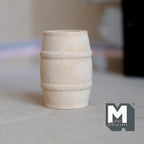 1:12 scale miniature wood wine barrel, medium, unfinished pale wood with raised bands, shown on a gray floor