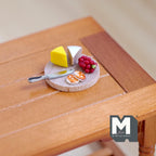 1:12 scale miniature cheese board with grapes and knife, round wood board with cheese wedges, shown on a wood table
